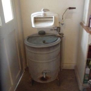 The copper looks like a steel barrel with a lid that opens on top and a tap to run off the used water at the bottom. It has a mangle with 2 rollers that are turned by a handle. The lid was left open to allow the wrung out water to return to the copper.